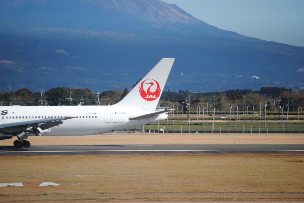 The tail of a Japan Airlines aircraft, the best airline to fly to Japan, on the tarmac with a mountain background.