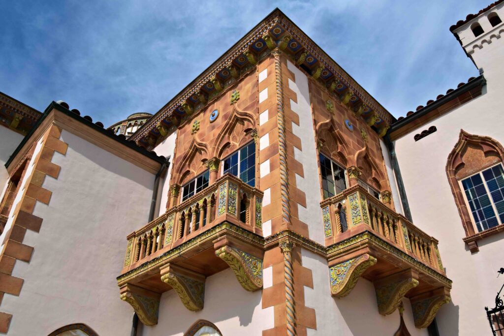 Ornate Venetian-Gothic balconies on a pink mansion's exterior.