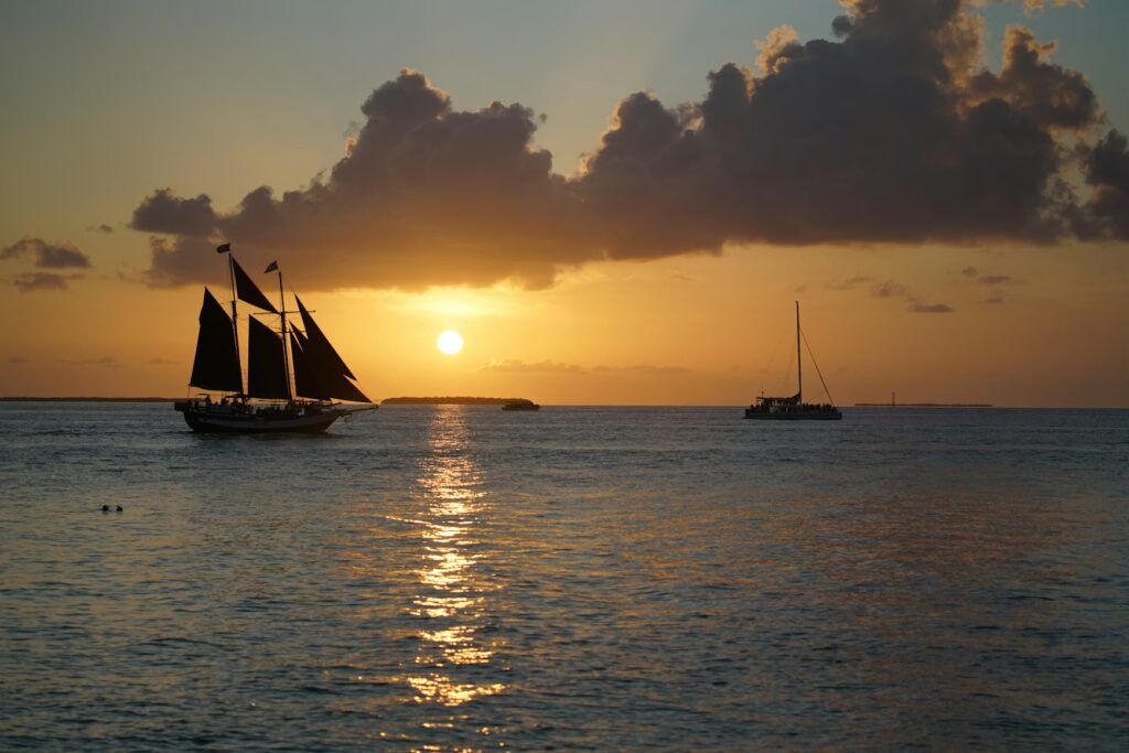 A beautiful sunset silhouette of a sailing ship and a catamaran on the water, highlighting the best time to visit Key West.