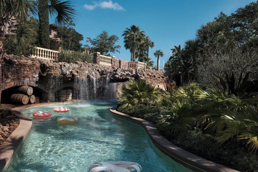 A serene lazy river with floating tubes drifting past stone bridges and waterfalls.
