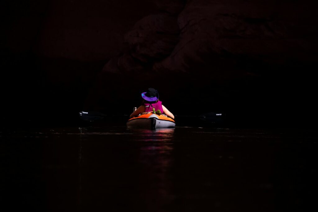 A lone kayaker silhouetted on the water at night, highlighting the peaceful experience of bioluminescent kayaking.