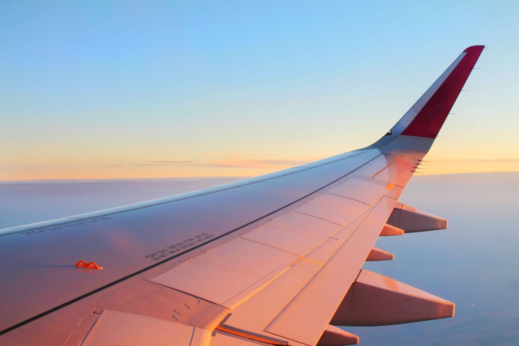 Airplane wing soaring above a thick layer of clouds during a beautiful sunset.