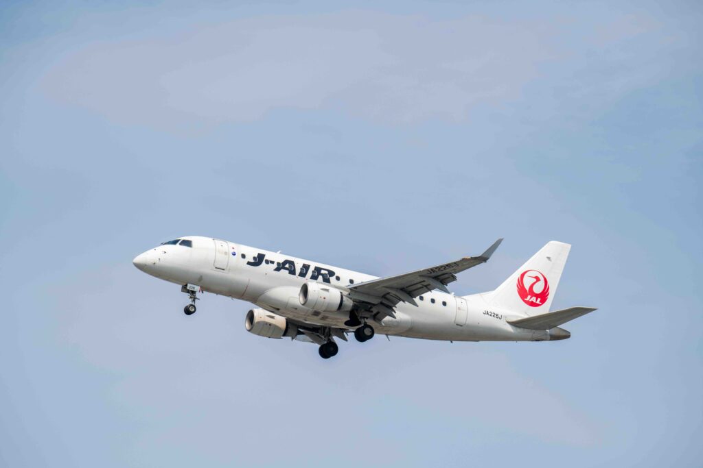 A white Japan Airlines airplane taking off against a clear blue sky.