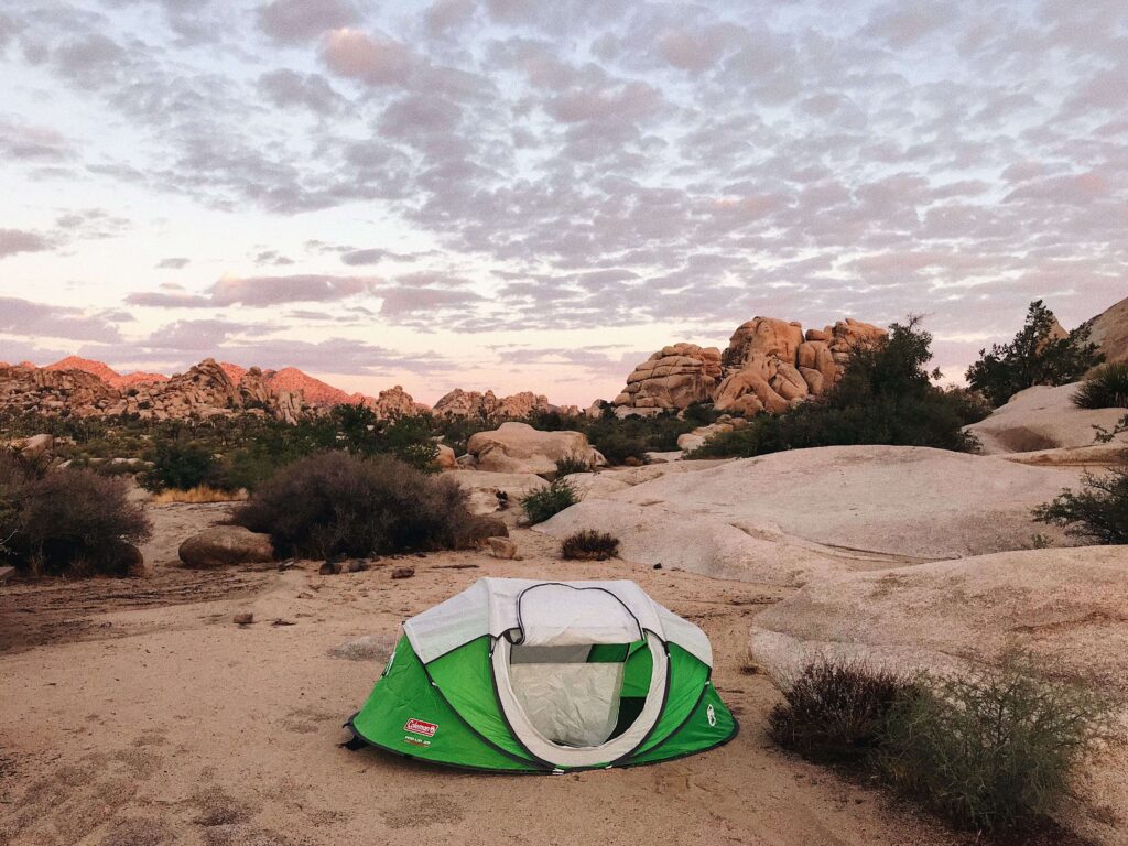 Green pop-up tent setup on sandy desert terrain near boulders at joshua tree tent sites.
