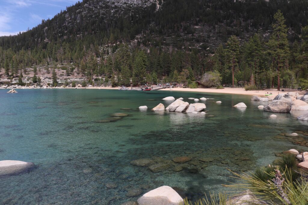 Turquoise water and white sand beach surrounded by pines at California beach campgrounds.