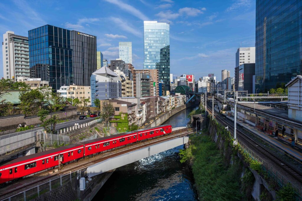 A bright red commuter train traveling on an elevated track through urban Tokyo.