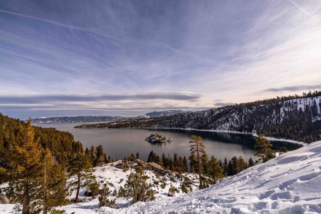 Snow covered slope overlooking clear blue lake bay at lake tahoe camping grounds.