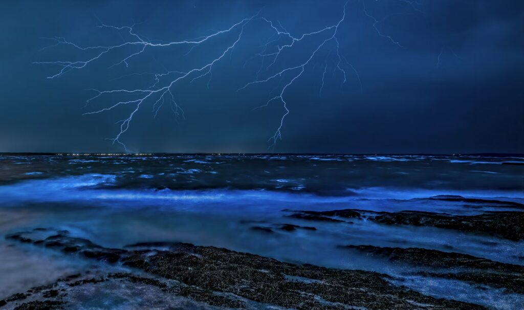 A bright lightning strike illuminating the night sky above a glowing blue ocean, showcasing the intensity of nature.