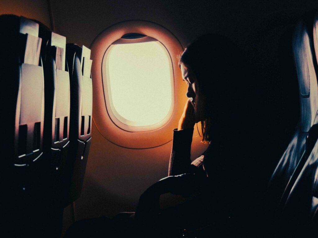 Silhouette of a passenger resting by the airplane window in a darkened cabin.