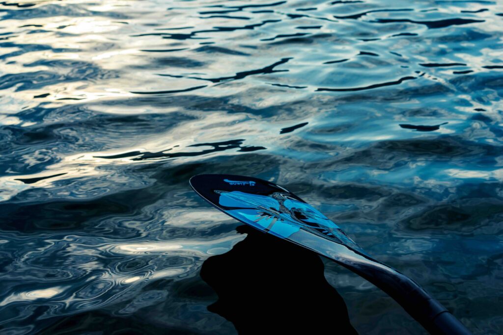 A close-up of a paddle blade reflecting a faint blue glow from the water.