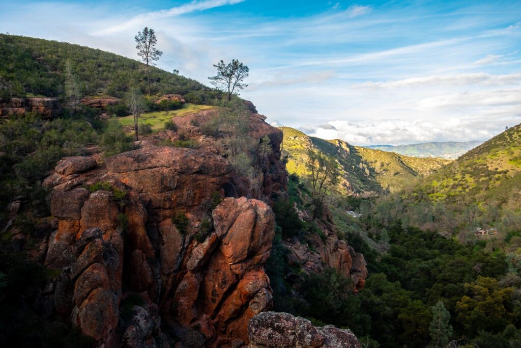 Volcanic rock spires rising over green trees and stream at pinnacles national park tent sites.