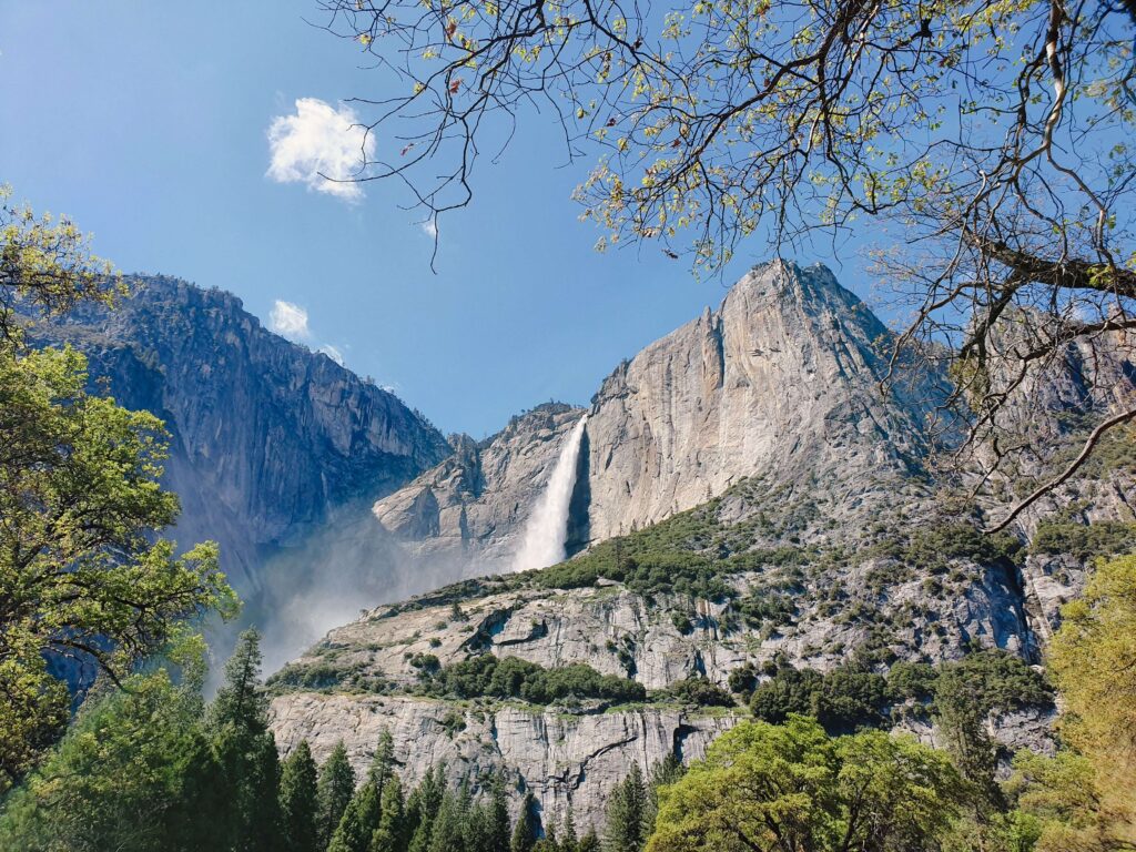 Green valley meadow and waterfall below granite cliffs at Yosemite national park camping.