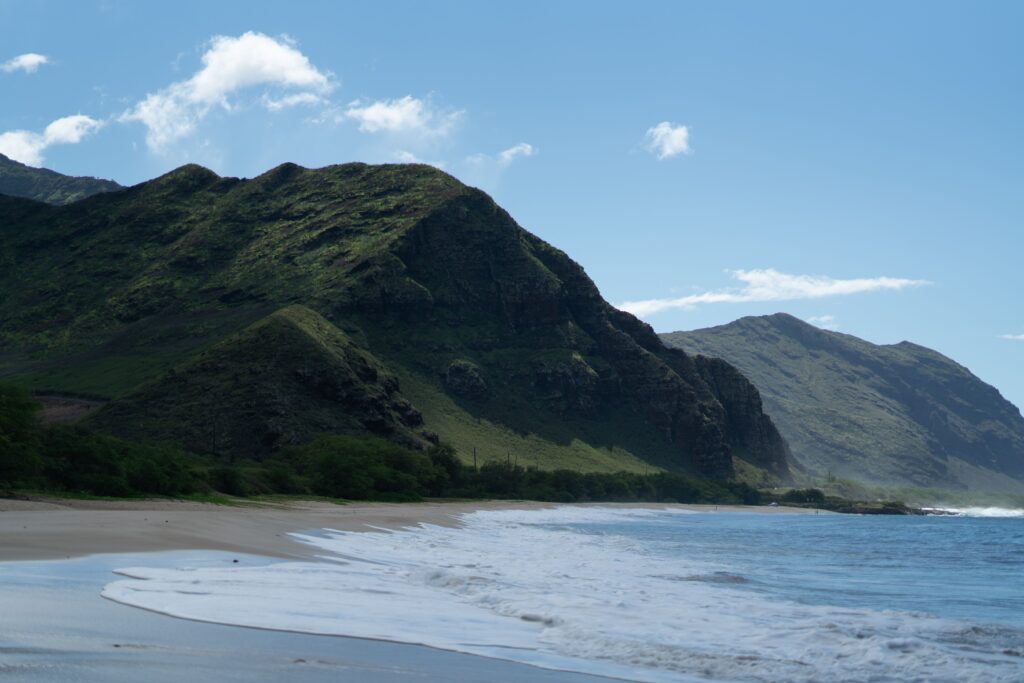 Wide sandy beach at the base of lush green mountain cliffs at hawaii coastal campsites.