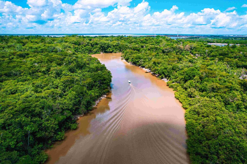 Aerial view of a boat navigating a winding brown river in the Amazon during the best season for Peru.