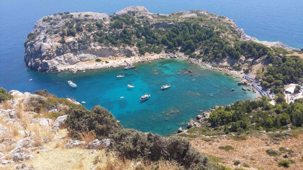 Pine covered rocky inlet surrounding emerald green water on Greece scuba beaches.