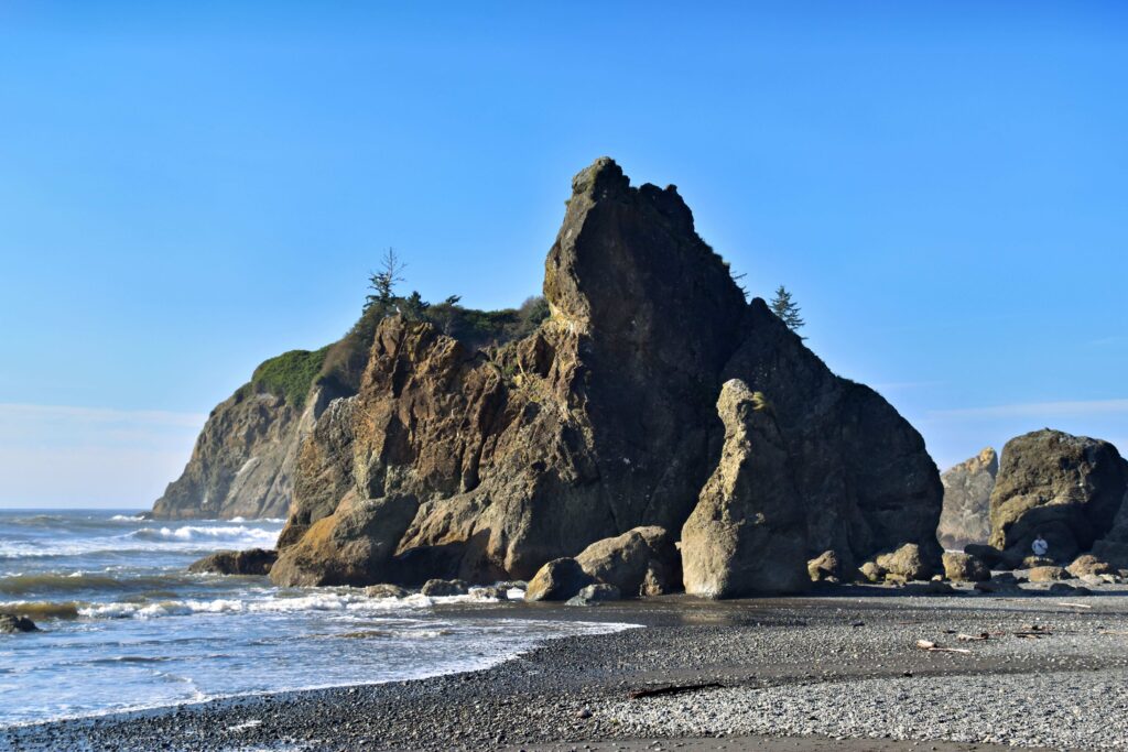 Rocky sea stack towering over dark sand shore at oceanfront camping spots.