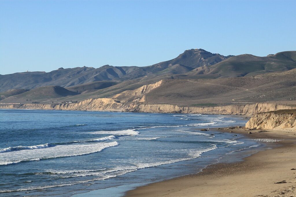 Ocean waves rolling onto sandy shore framed by hills at secluded shoreline campsites.