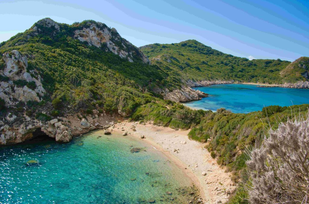 21 Best Beaches in Greece: Sandy Shores & Hidden Coves Aerial view of blue sea and green coastline showing best beaches in Greece.