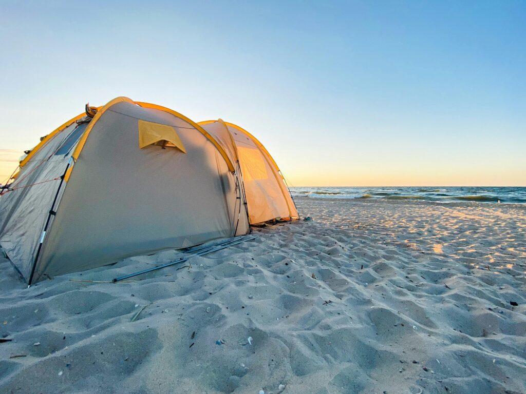 Best Beach Camping in the US (2026): 15 Epic Sites & Tide Rules A white tent pitched on a sandy shore facing the sea for beach camping.