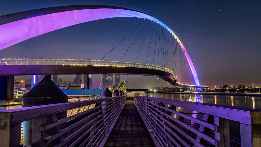 Pedestrian Tolerance Bridge glowing with purple LED lights over Dubai Canal at night, top best spots in dubai.