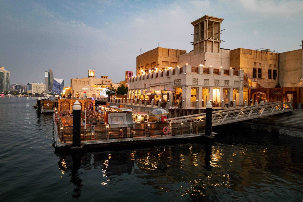 Outdoor evening restaurant tables on wooden deck beside Madinat waterways, one of the top places for dinner.