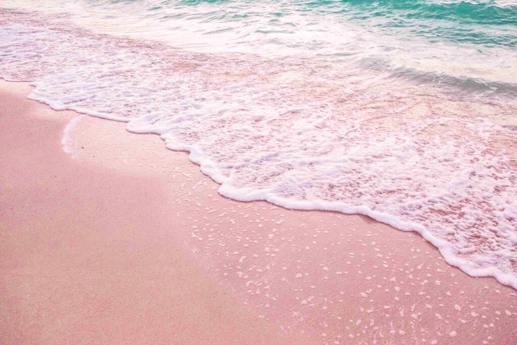 Pink sand shore washed by gentle clear turquoise waves on beautiful Greece beaches.