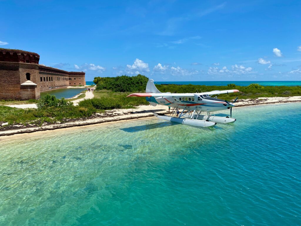 Seaplanes parked on turquoise beach beside historic fort brick walls at island tent camping.