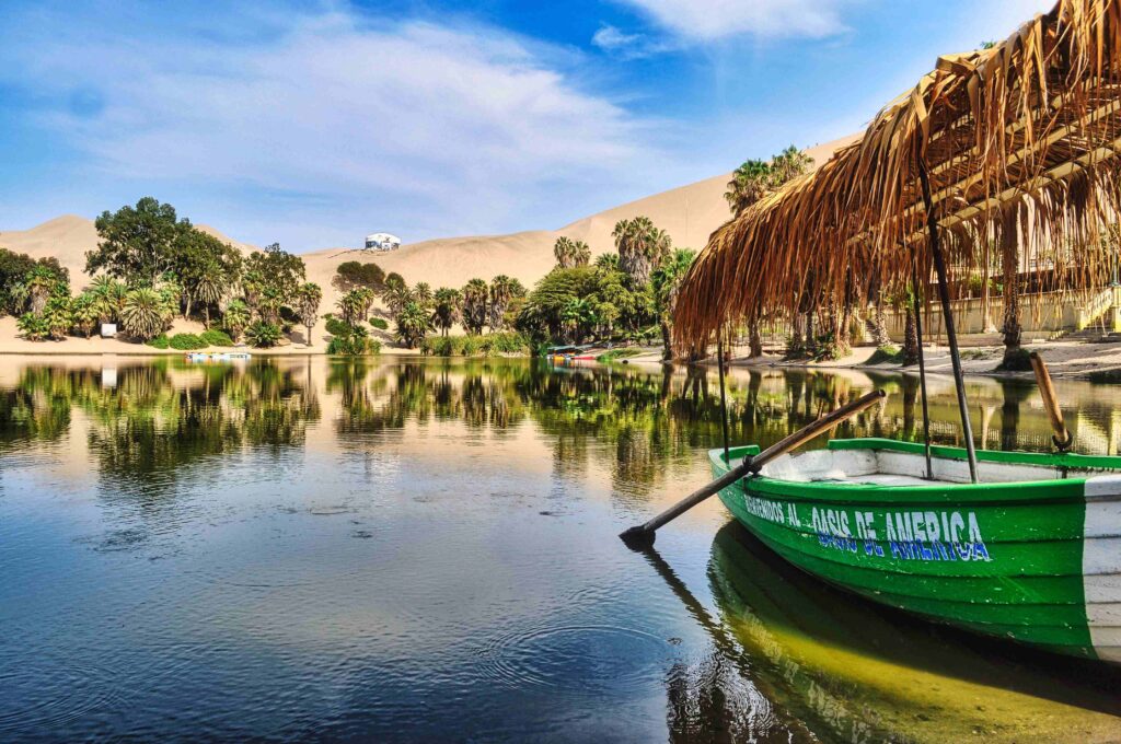 Tranquil desert oasis lagoon surrounded by palm trees and high Peru dunes.