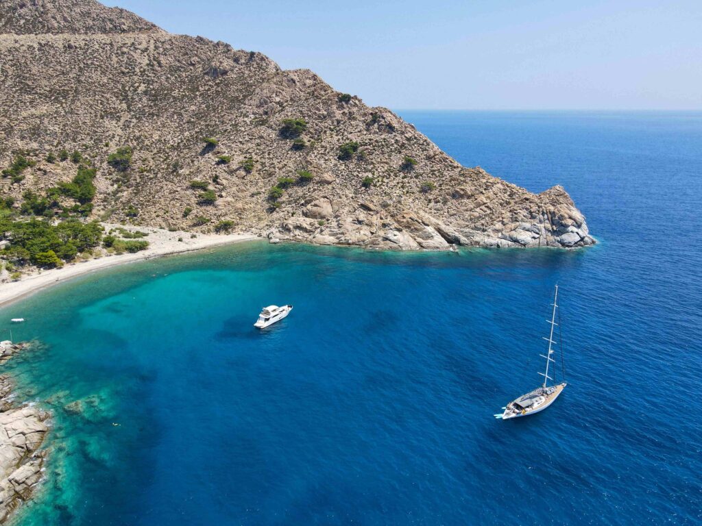 Yacht anchored in a clear blue bay of Ikaria, known as affordable Greek islands.