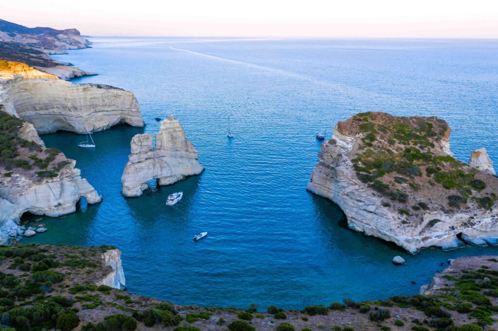 White volcanic rock arches over deep blue sea water when visiting Greek islands.