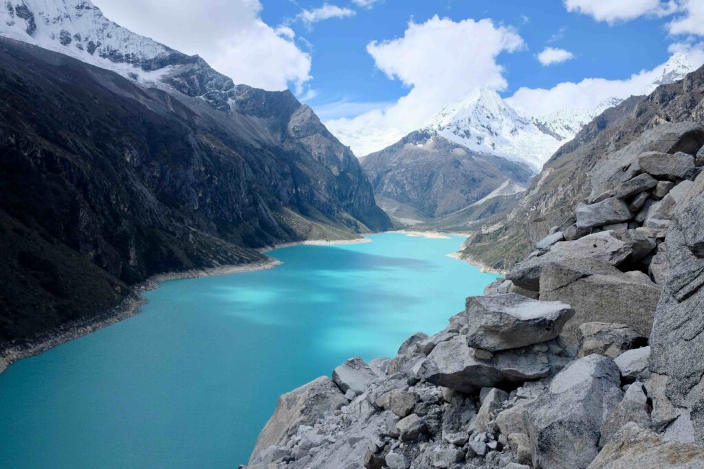 Bright cyan turquoise glacier lake framed by snow capped mountain peaks in Huaraz, Peru.