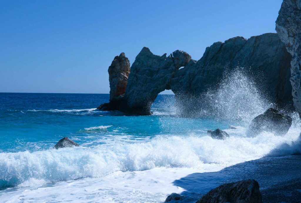 Waves crashing through a natural rock arch in the sea at unique Greece beaches.