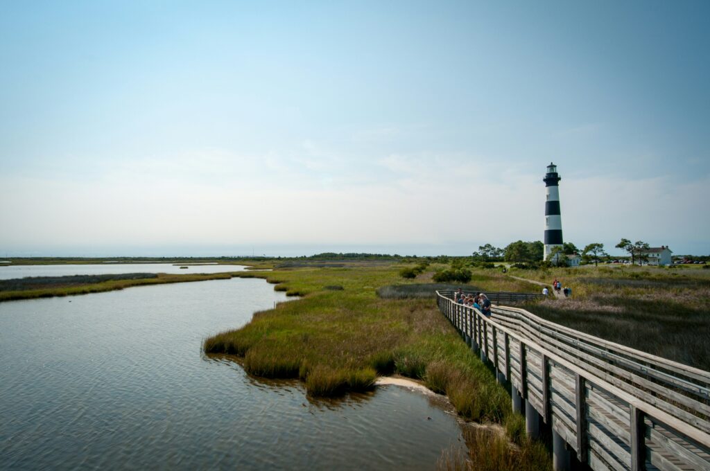 Wooden boardwalk leading to striped lighthouse at atlantic beach grounds.