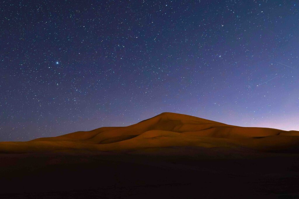 Starry night sky glowing above serene desert sand dunes, one of the best spots in dubai for overnight camping.