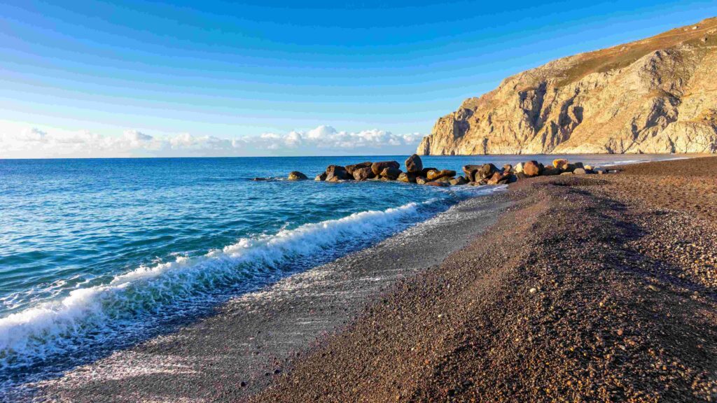 Waves crashing on black volcanic sand shore at the best beaches in Greece.