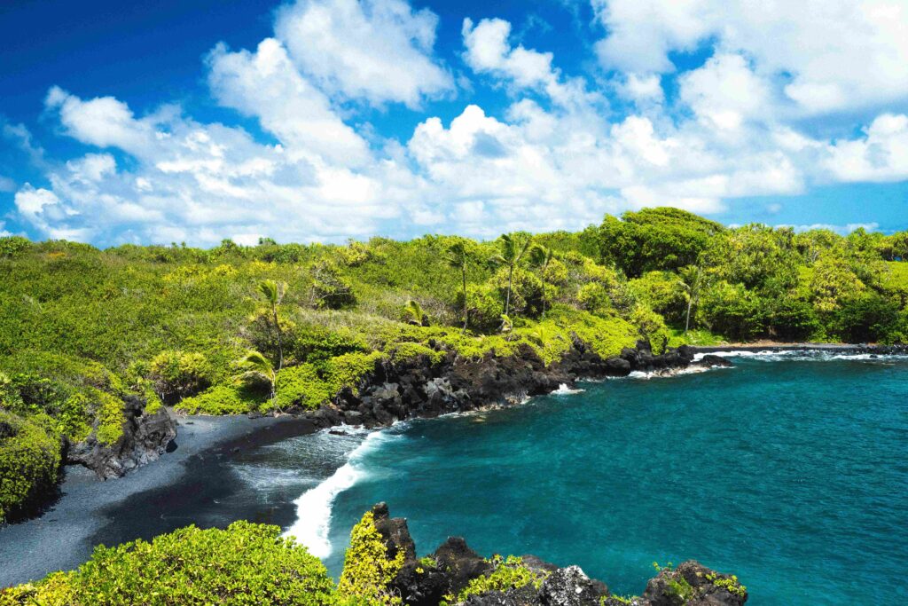 Volcanic black sand cove surrounded by green tropical hills at black sand camping spot.