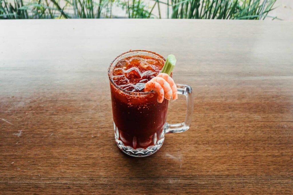A glass mug of a Bloody Mary with a spicy rim, garnished with shrimp and celery. Source: Unsplash