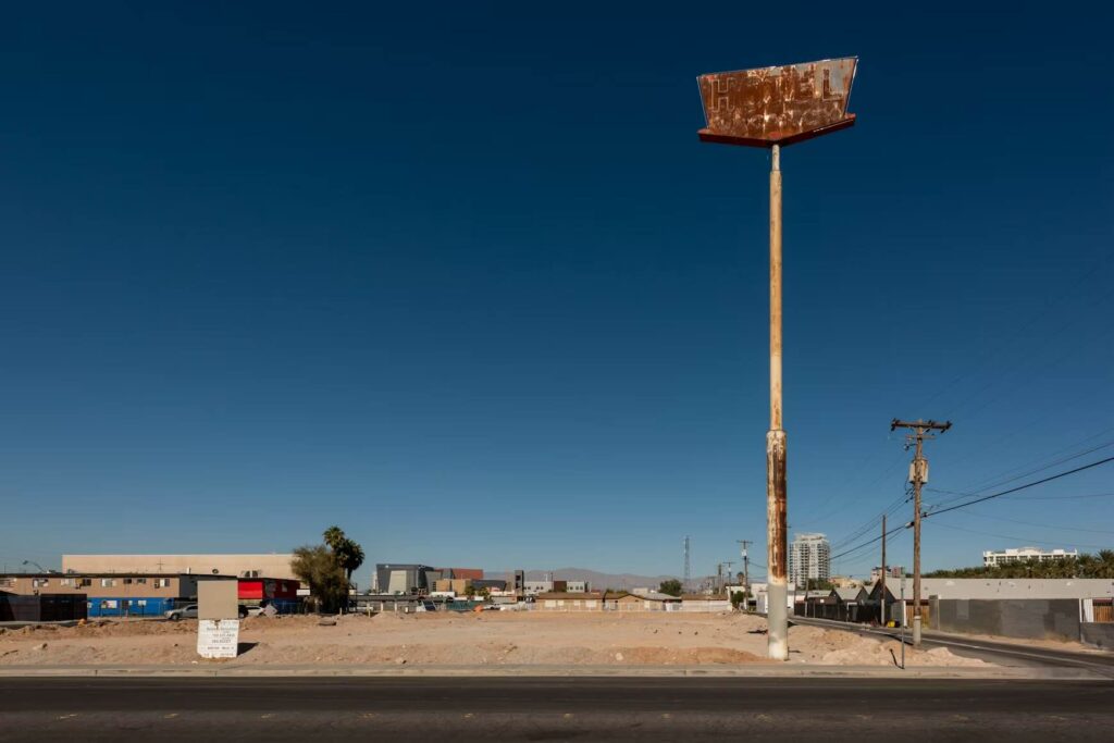 An empty, dirt lot with a tall, rusted signpost under a clear blue sky. - Source: Unsplash